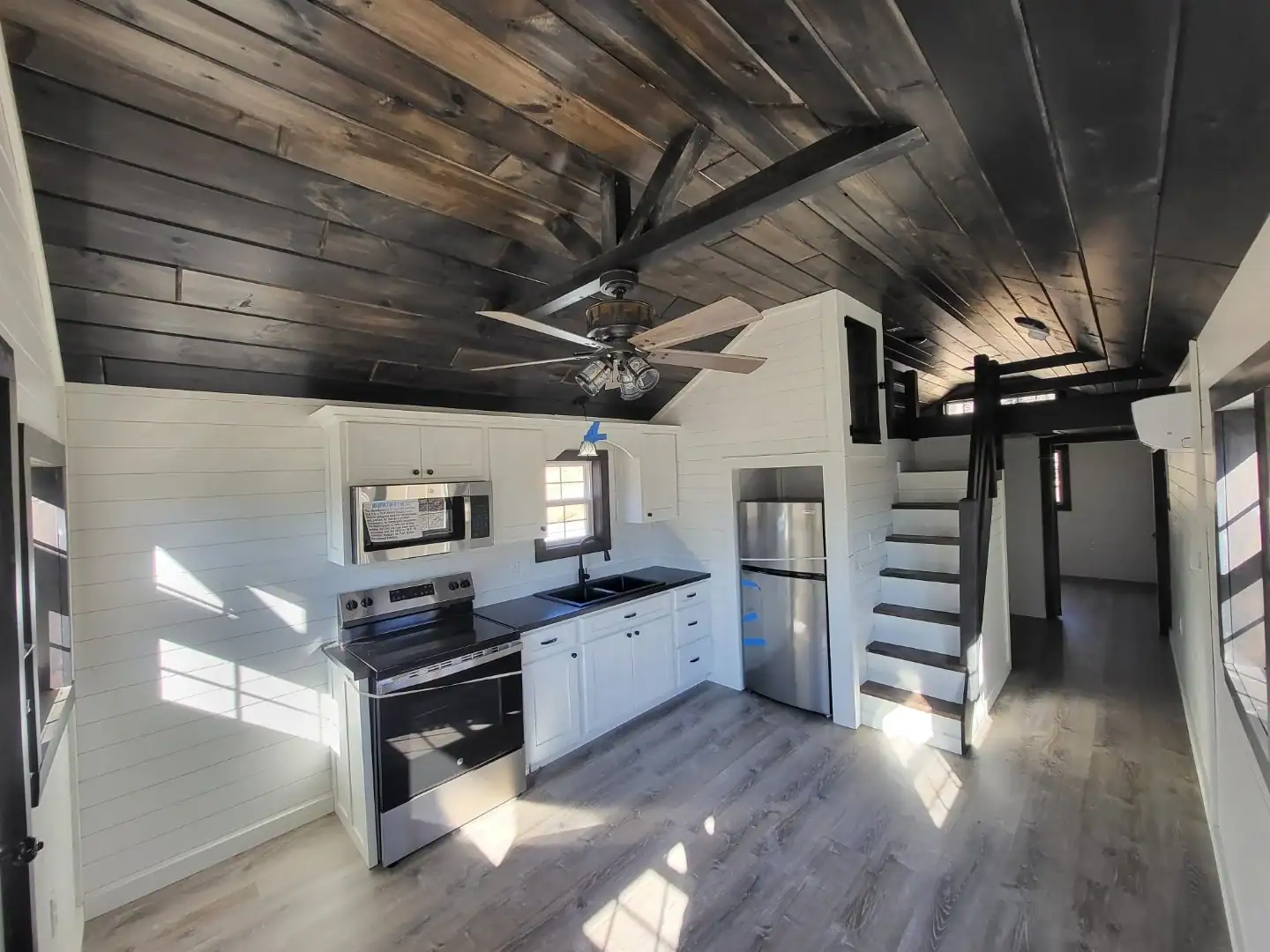 Woodland cottage kitchen with white cabinets, stainless range and refrigerator, and a staircase climbing to the loft
