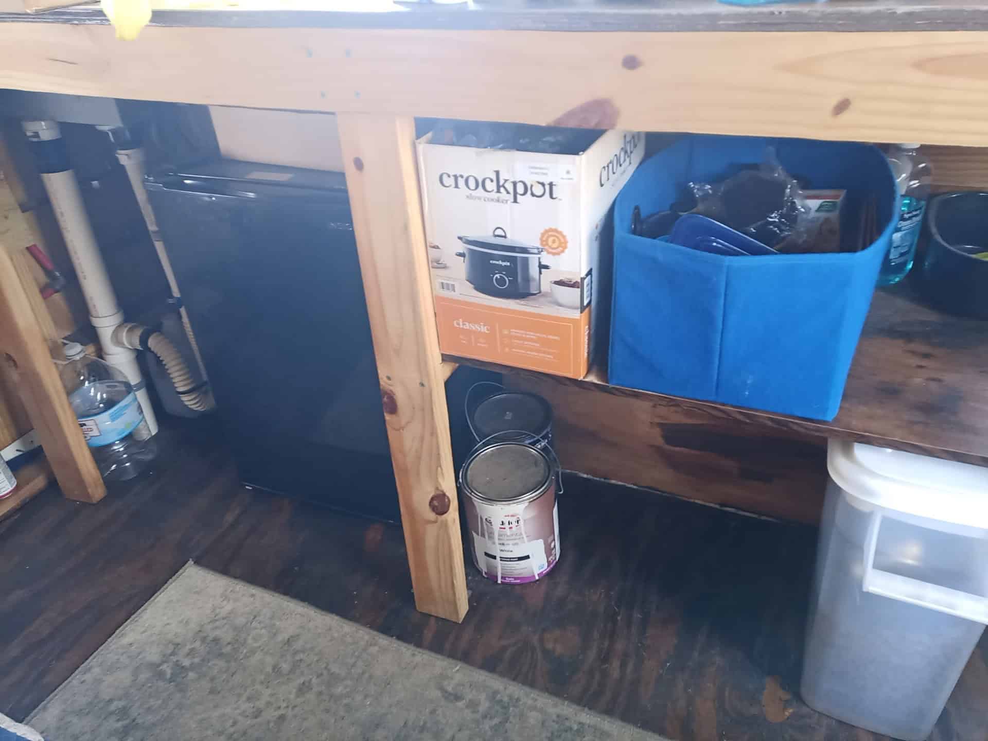Under-counter space with a compact fridge, unfinished wood frame, PEX water lines, and a PVC drain