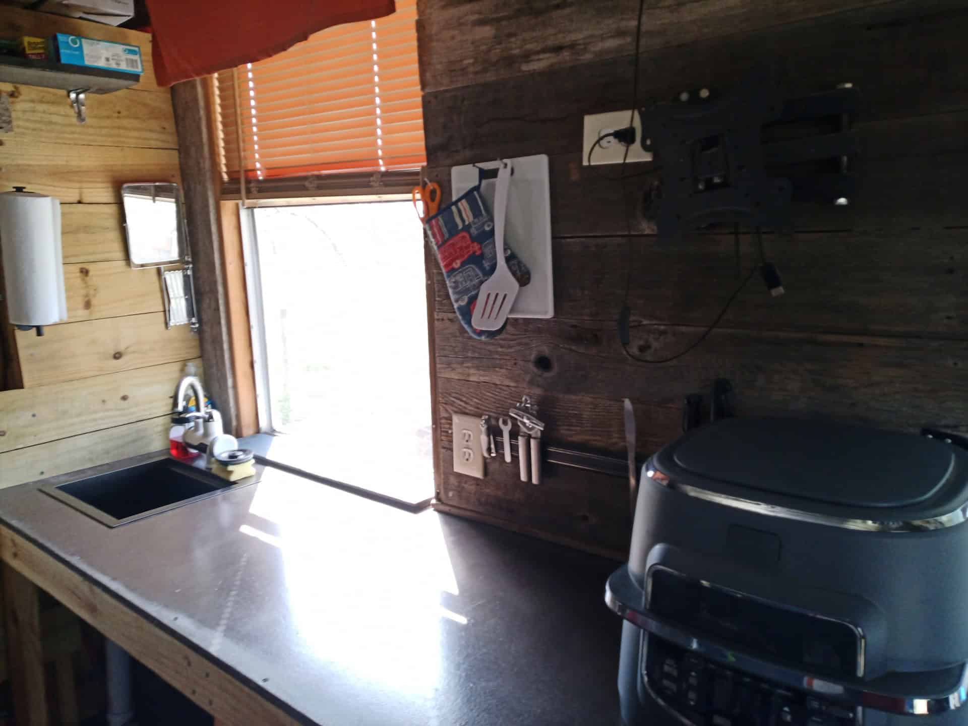 Kitchen counter with a square sink and gooseneck faucet under a large window with orange blinds