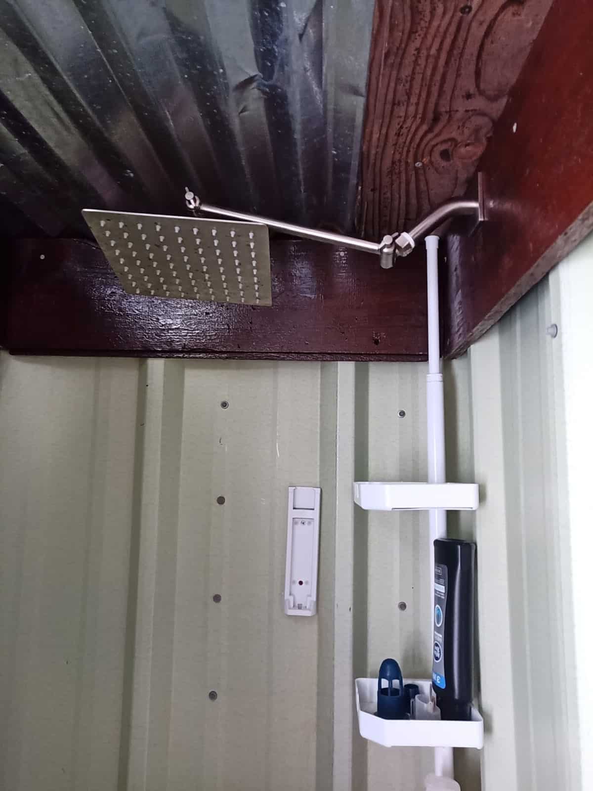 Square rainfall shower head on a swivel arm above pale green corrugated-metal shower walls