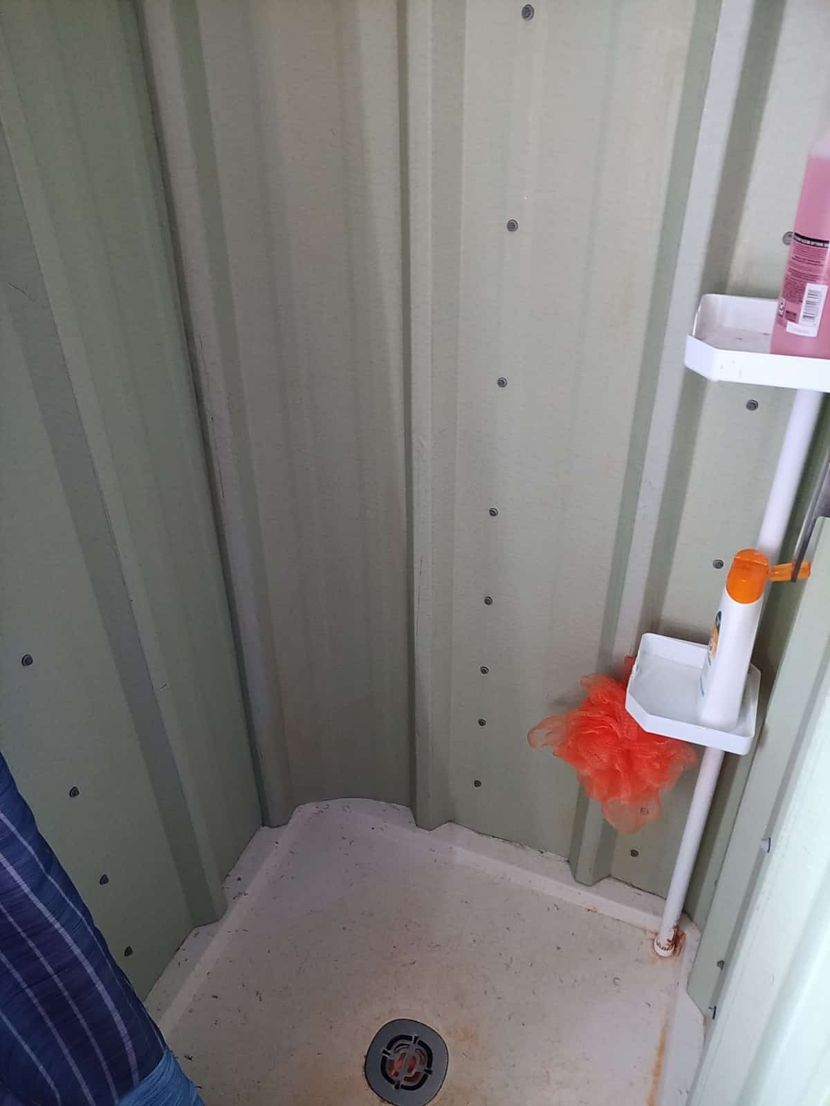 Full-size shower stall with pale green corrugated-metal walls and a white square shower pan
