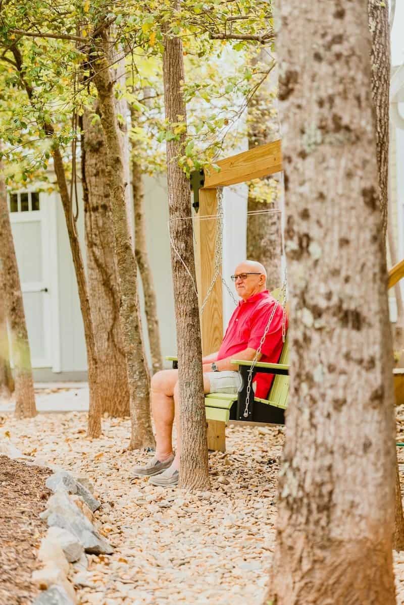 A resident in a red shirt relaxes on a porch swing among tall pines