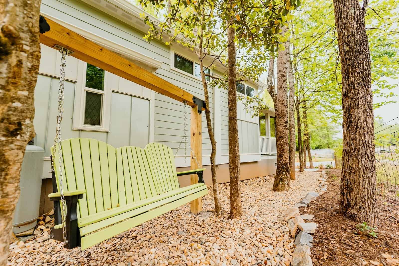 Lime-green porch swing hanging from a wooden frame beside a cottage in the woods