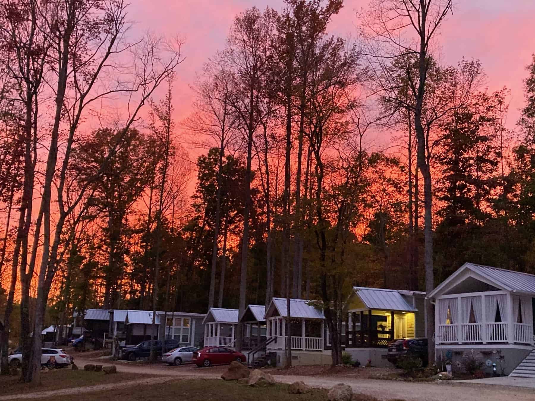 A row of park-model cottages with lit porches under a pink and orange sunset sky