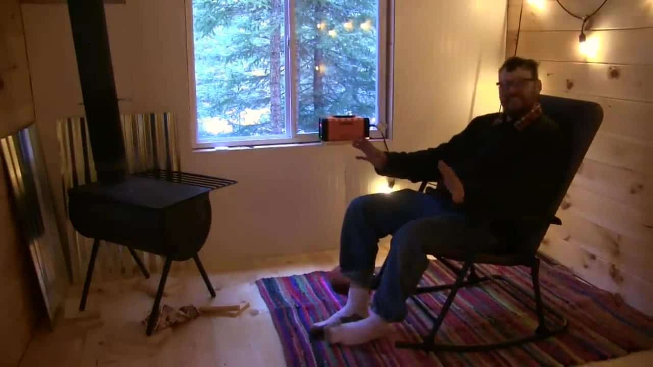 Finished tongue-and-groove interior with Dave in a rocking chair, wood stove, and snowy window