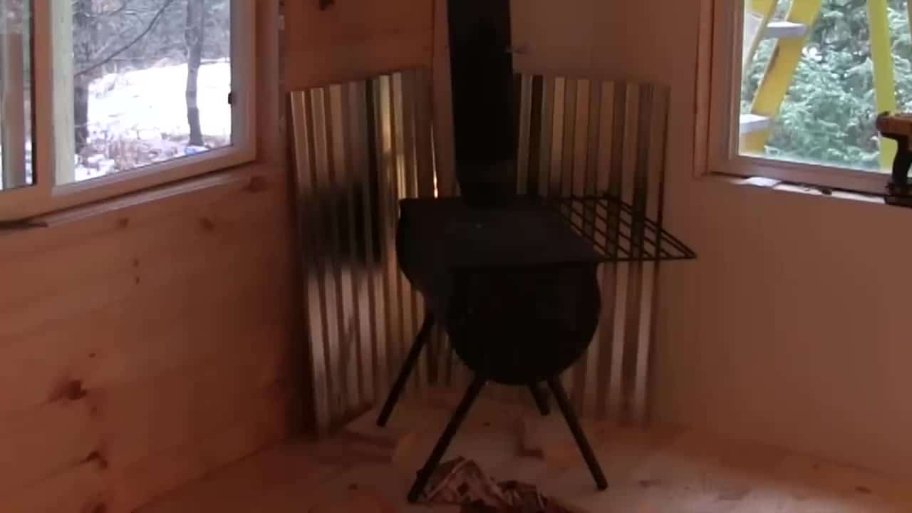 Barrel wood stove close-up with corrugated heat shield in the 10x16 cabin
