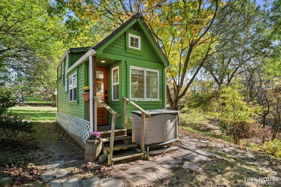 Green tiny house on wheels with modern architecture and large windows.