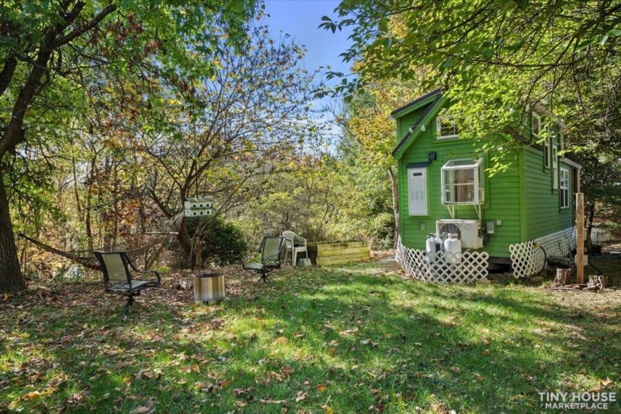Compact green tiny house on wheels surrounded by trees and nature.