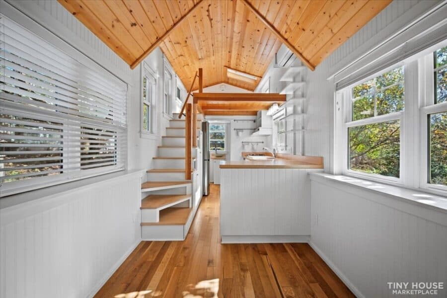 Bright tiny house interior with wooden ceiling, white walls, and large windows for natural light.