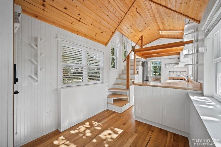 Cozy tiny house interior with white walls, wooden ceiling, and large windows for natural light.