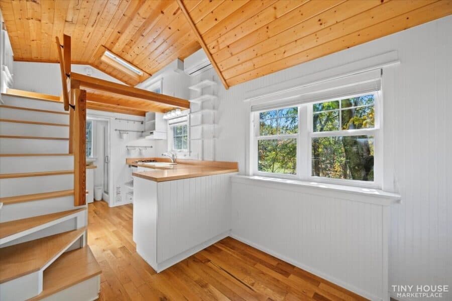 Interior of architect-designed tiny house on wheels with natural wood accents and large windows.