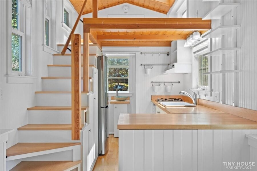 Modern tiny house interior with compact kitchen and staircase on wheels.