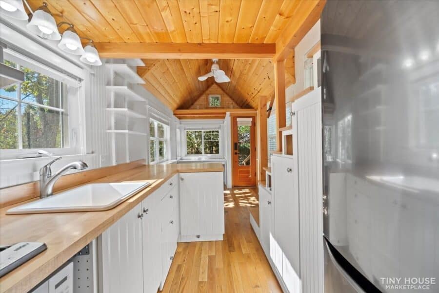 Bright tiny house kitchen with white cabinets and natural wood accents.