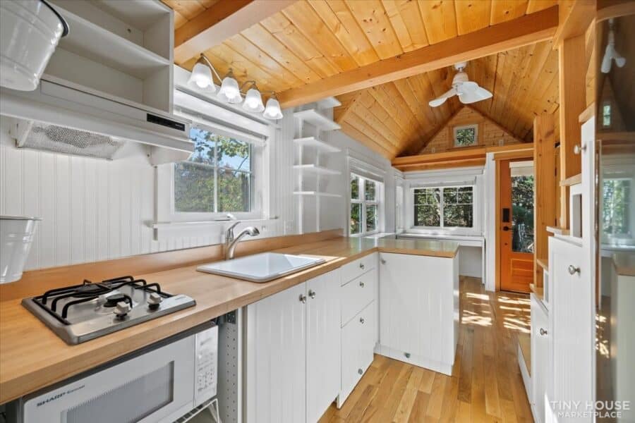 Bright tiny house kitchen featuring white cabinets and wooden accents.