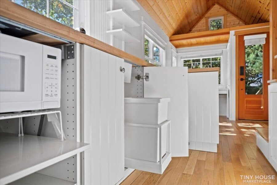Bright tiny house interior with white panel walls, natural wood ceiling, and compact kitchen space.