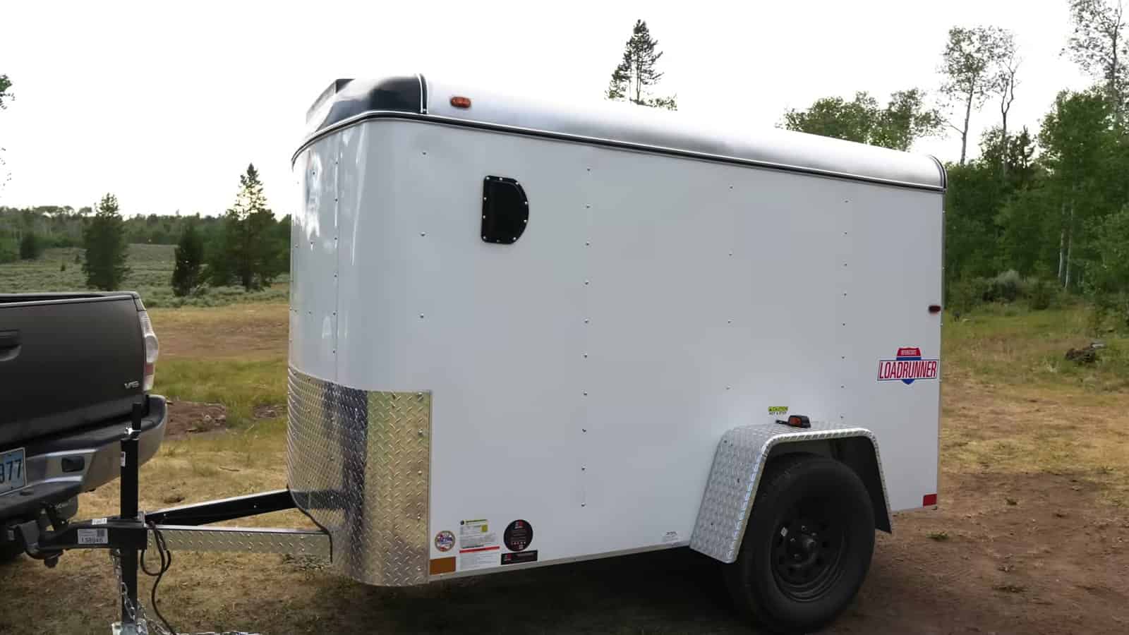 Brand-new white 5x8 cargo trailer hitched to a pickup in a Wyoming meadow