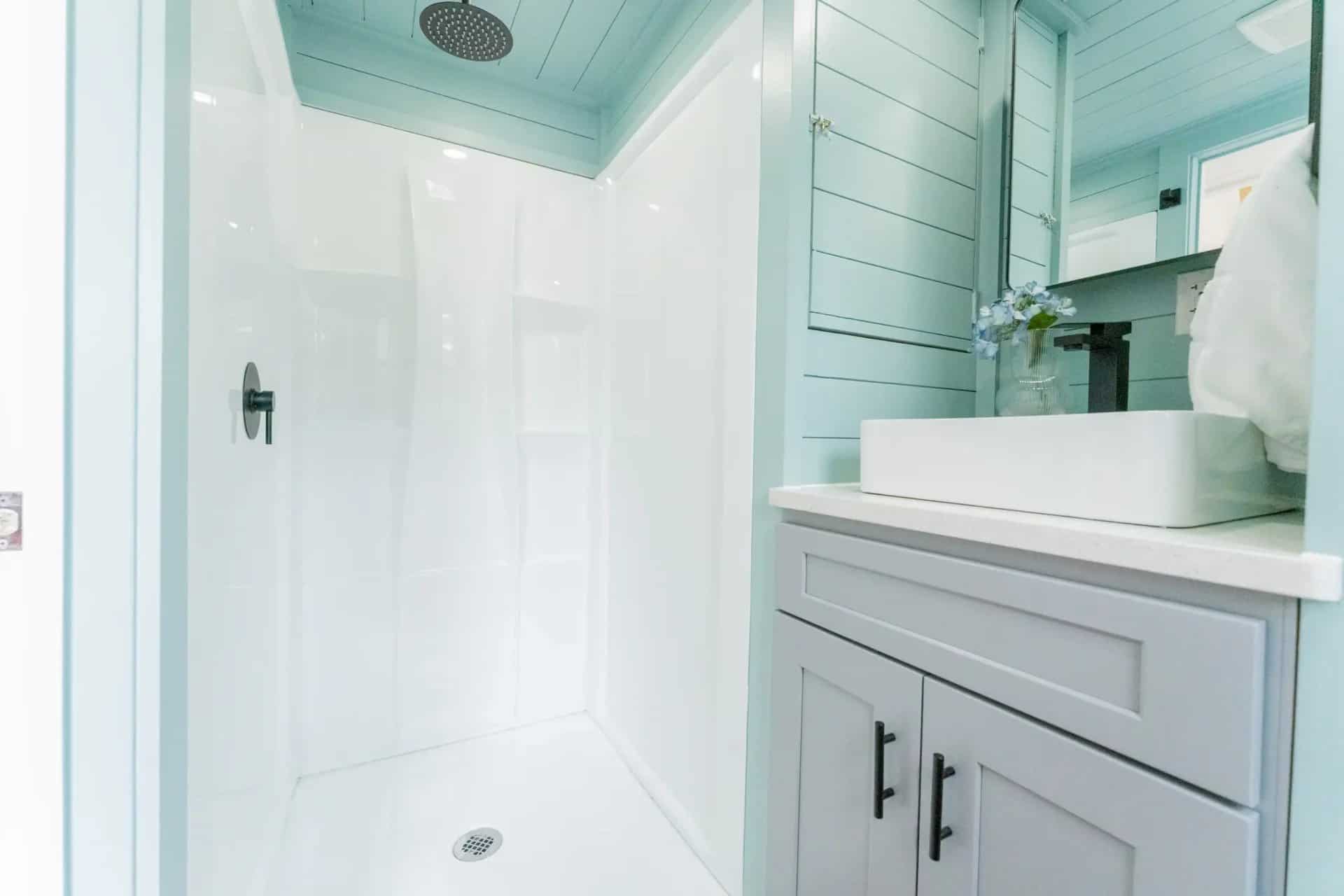 Walk-in shower with rain showerhead beside a gray vanity in the Avalon 24 bathroom