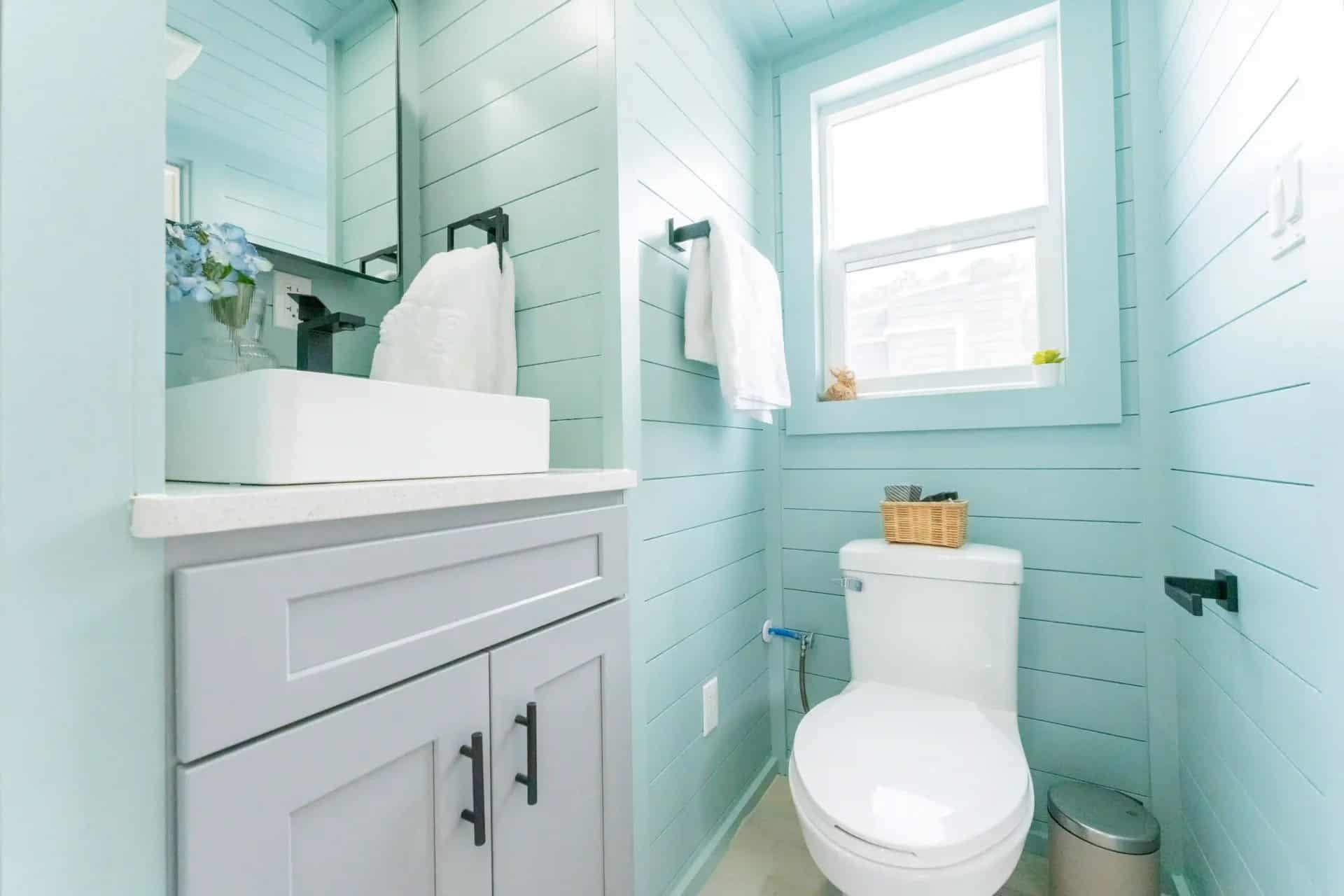 Avalon 24 bathroom with gray vanity, vessel sink, flushing toilet, and window