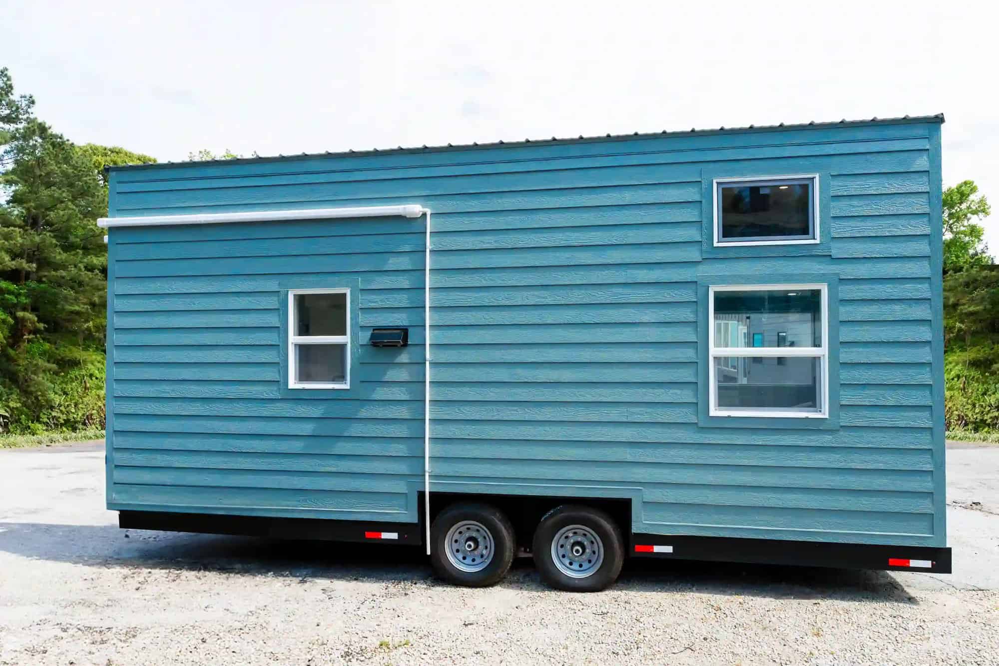 Side of the blue Avalon 24 tiny house on wheels with small windows and a metal roof
