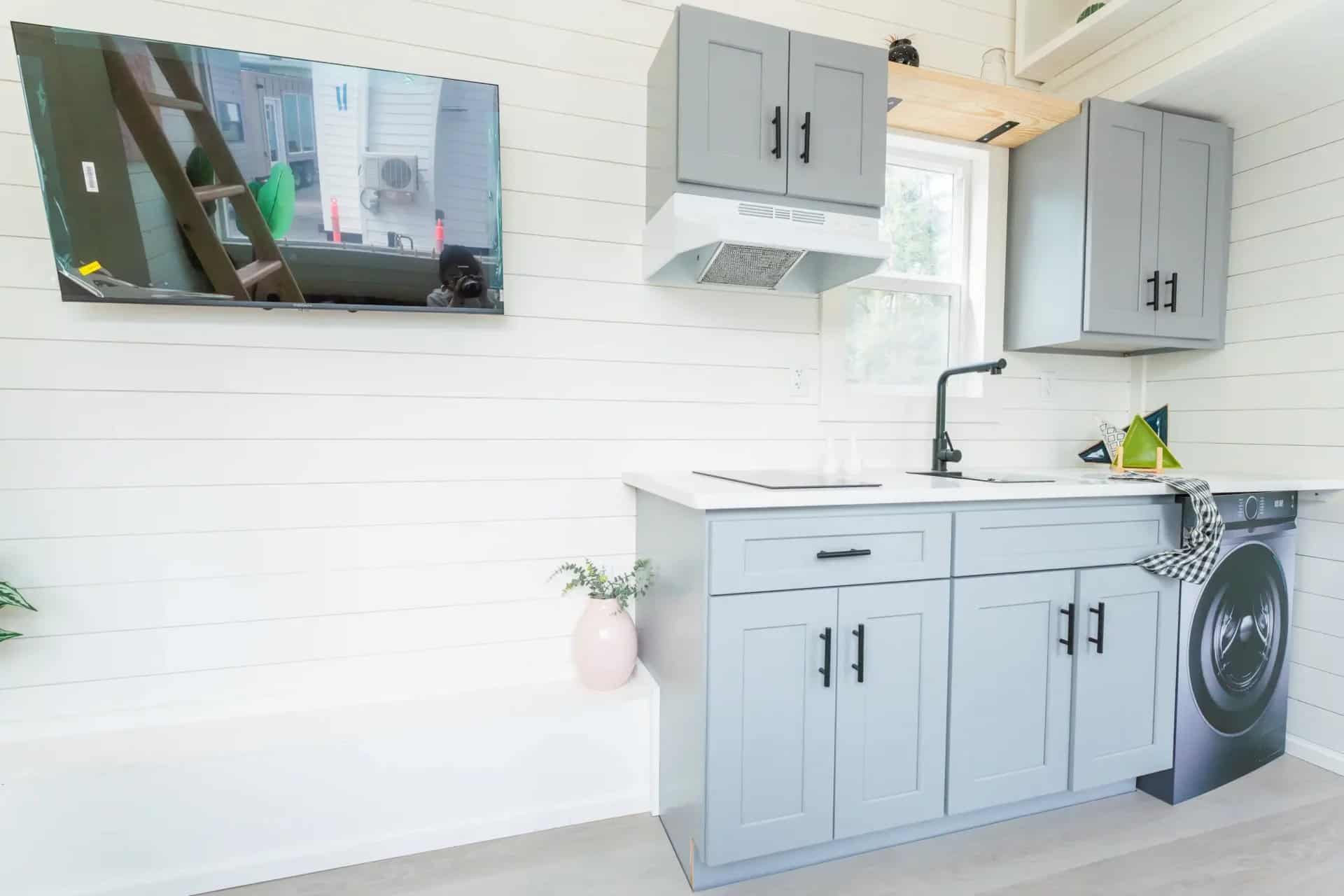 Avalon 24 kitchen counter with sink and washer/dryer combo below, wall-mounted TV opposite