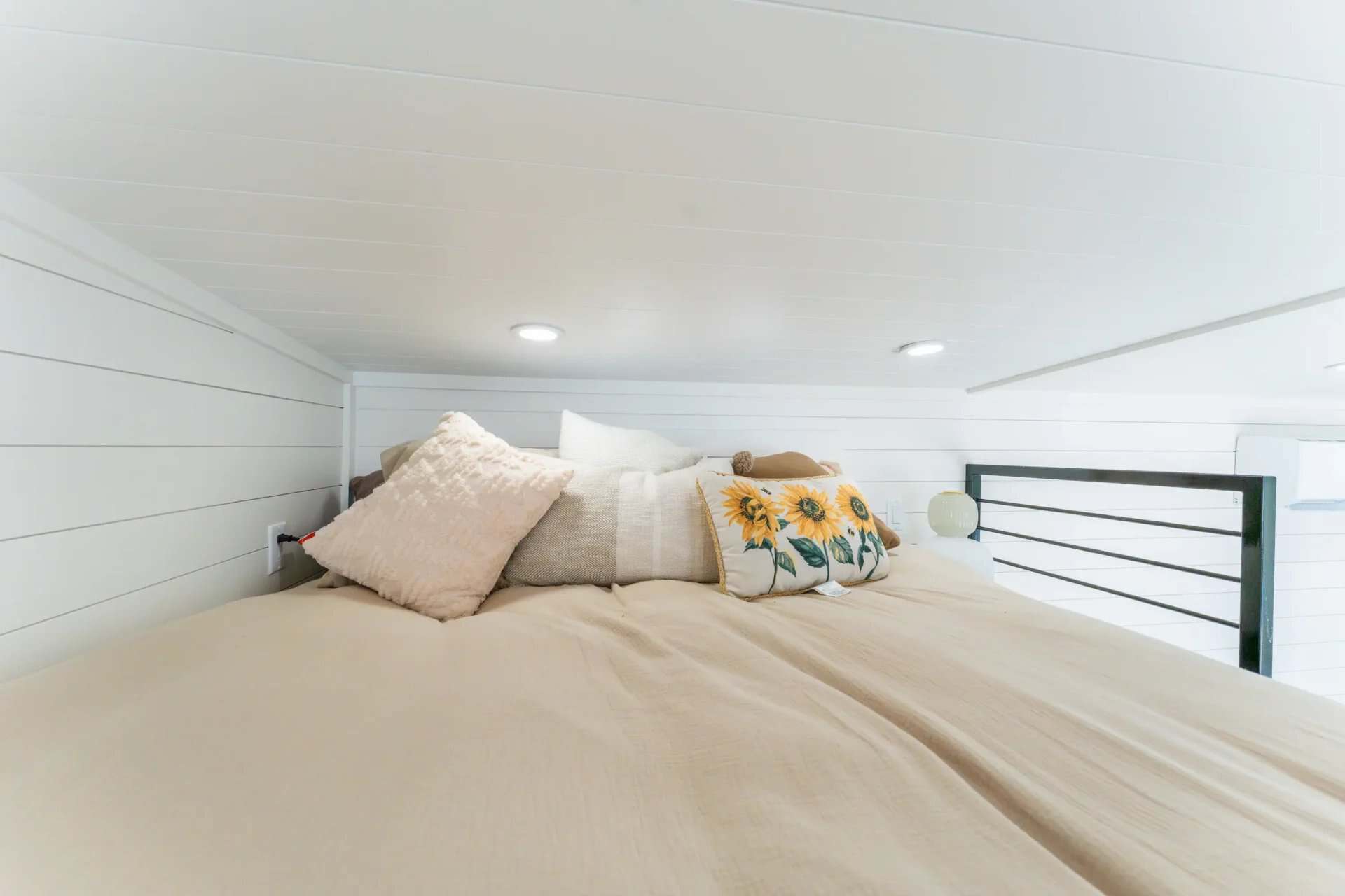 Main sleeping loft in the Avalon 24 with a double bed, sunflower pillows, and metal safety railing