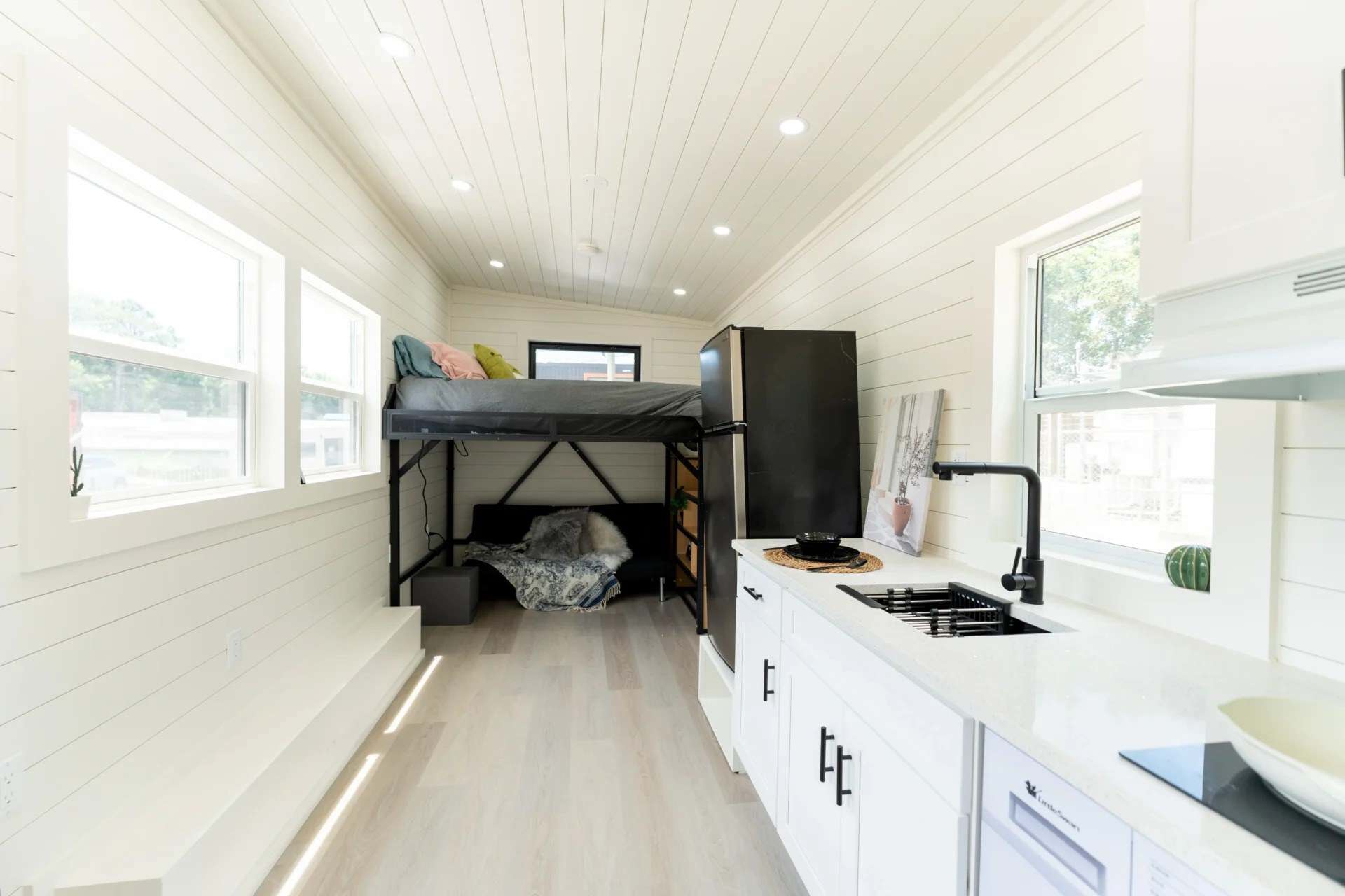 Fairfax gallery interior: white shiplap, kitchen with black sink and fridge, lofted bed at the far end, light plank floor