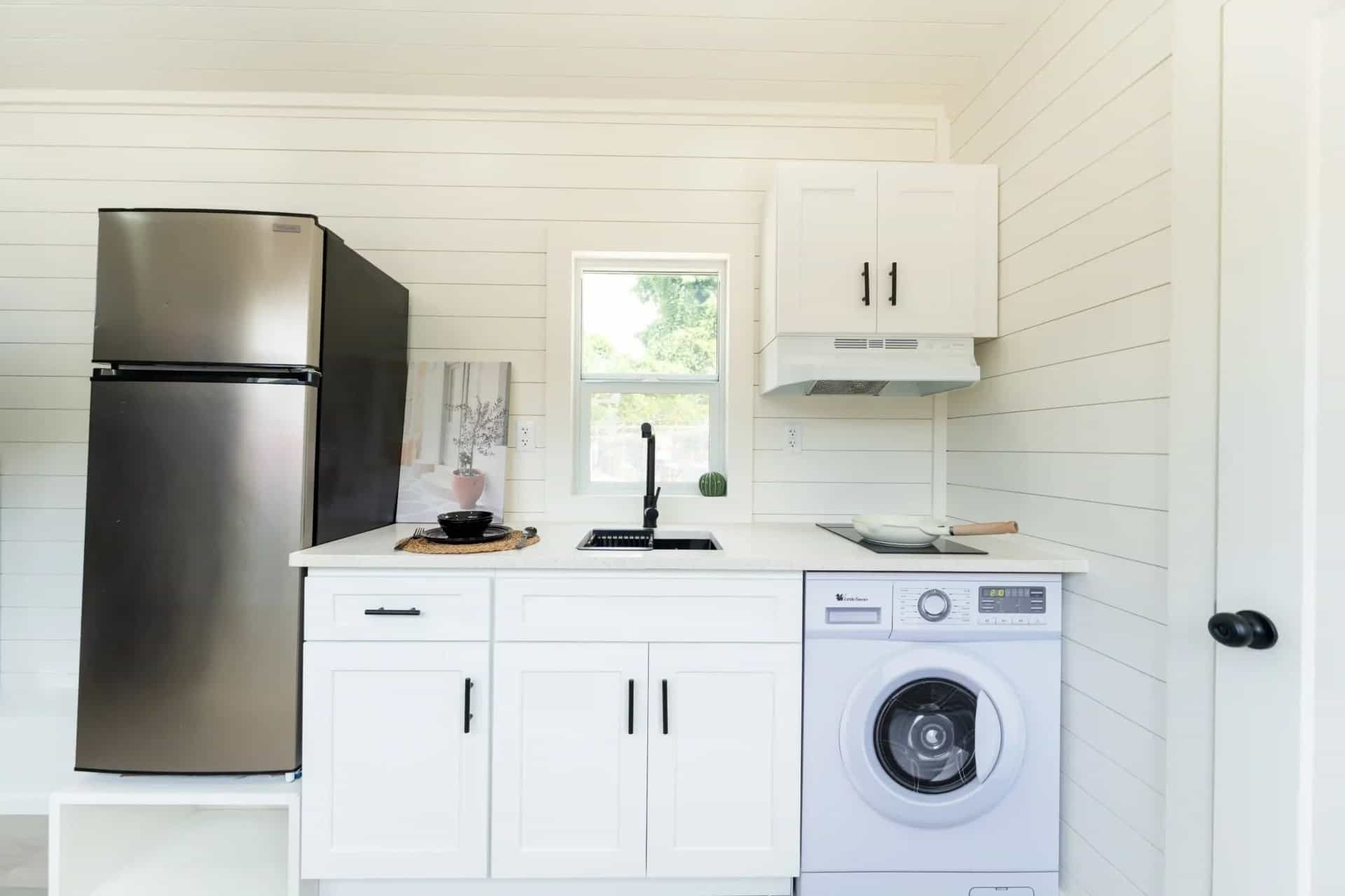 Fairfax gallery kitchen: white cabinets, black faucet and two-burner cooktop, stainless fridge, combination laundry under the counter