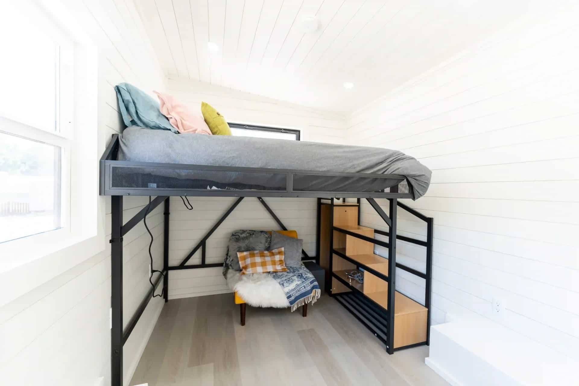 Fairfax gallery lofted bed: black metal loft frame, grey bedding, storage stairs with cubbies, seating under the loft