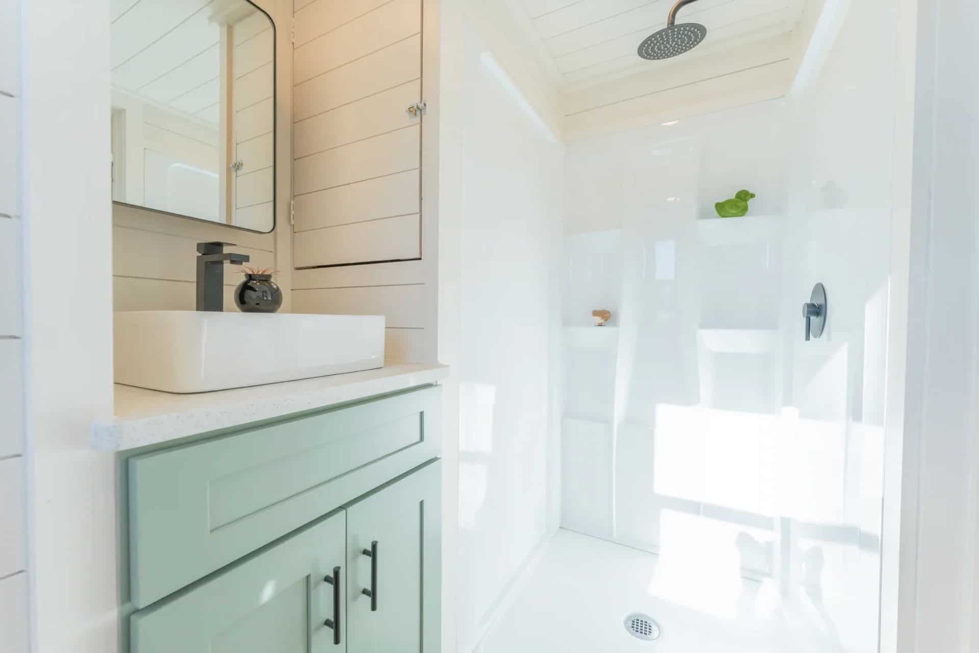 Genesis gallery bathroom: mint vanity with vessel sink, black faucet, mirrored cabinet, and a white shower with a rainfall head and niches