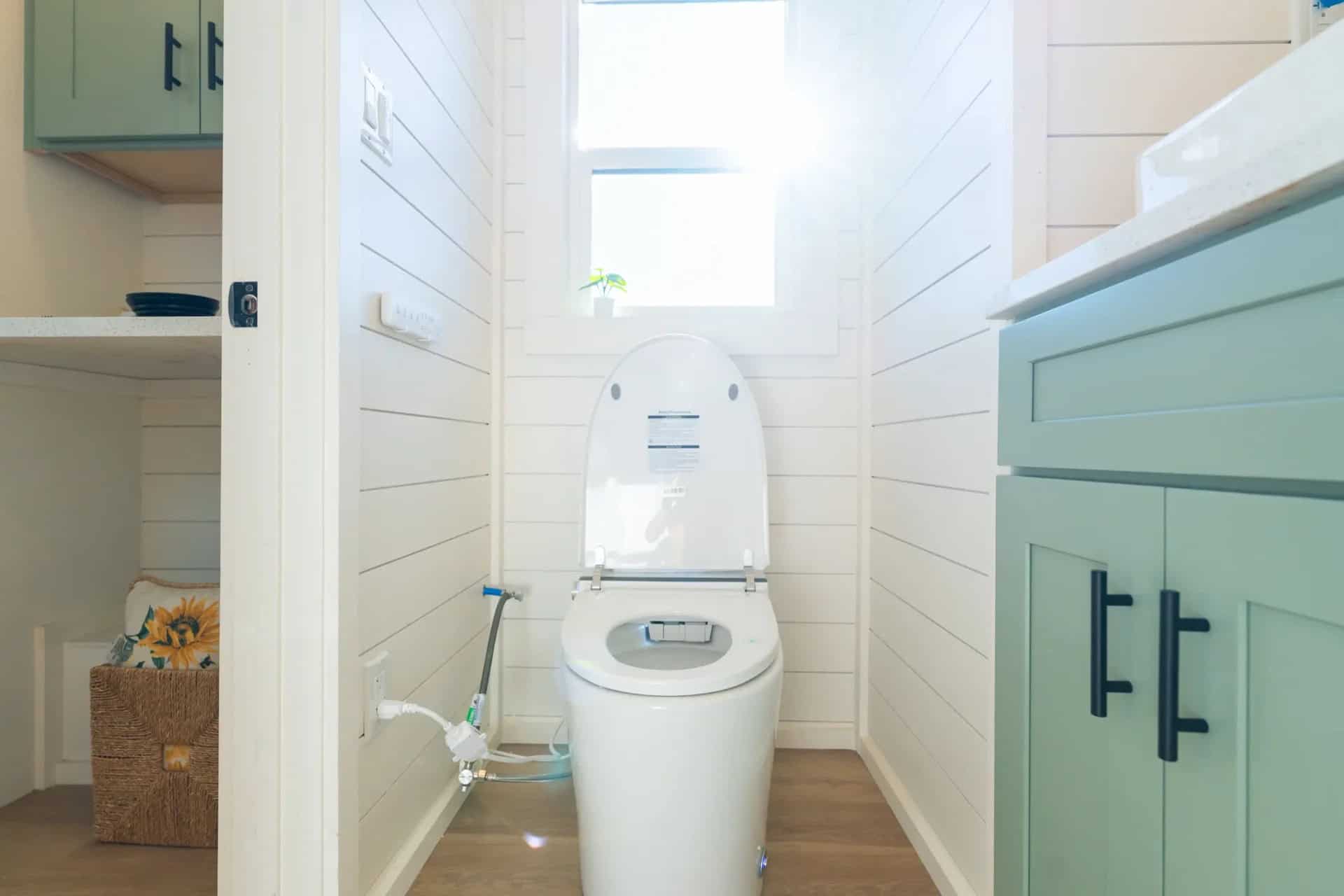 Genesis gallery: view from the bathroom doorway to the flush toilet under the window, mint vanity at right, kitchen shelving visible through the door