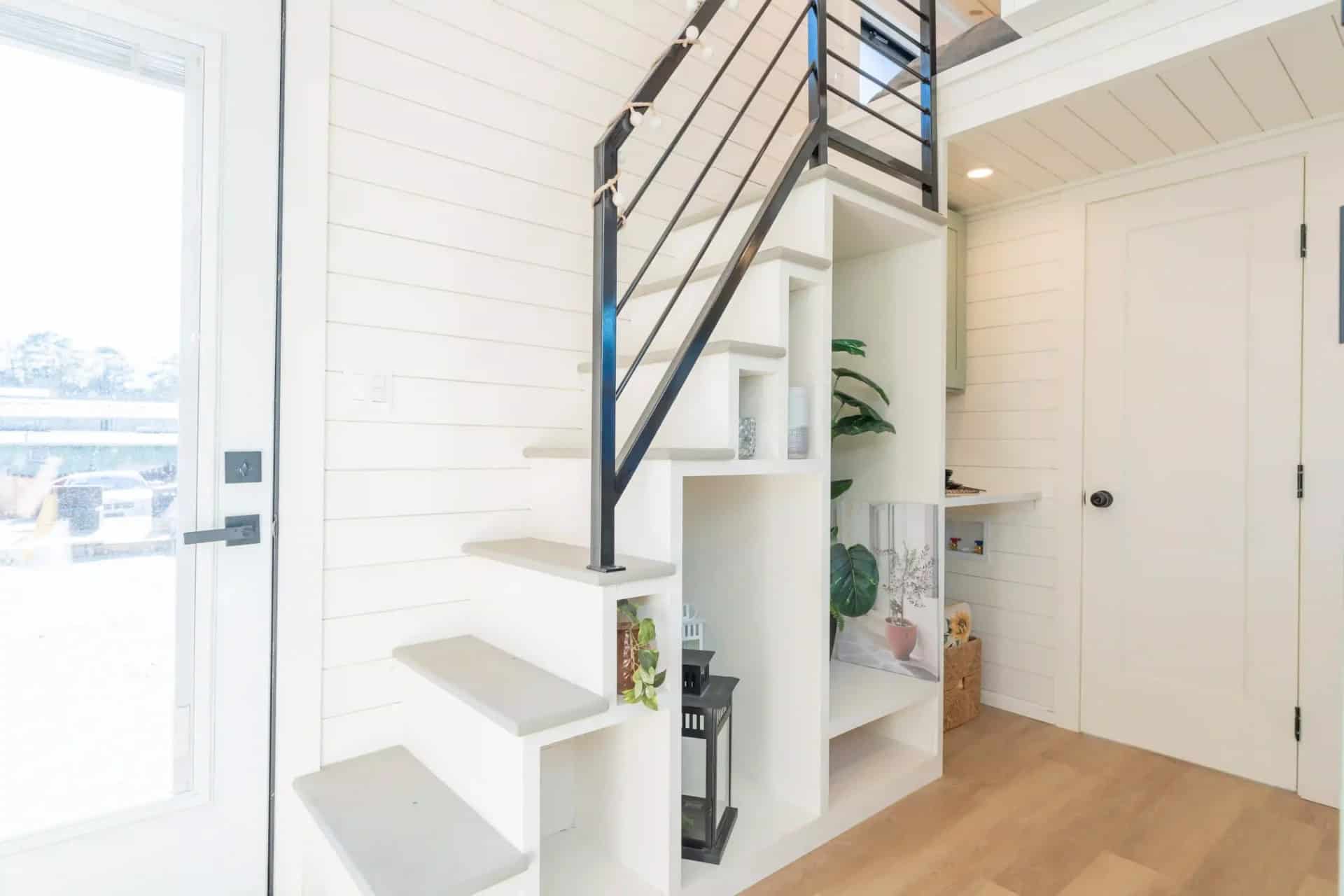 Genesis gallery interior: white storage stairs with open cubbies and a black metal rail beside the glass entry door, loft above