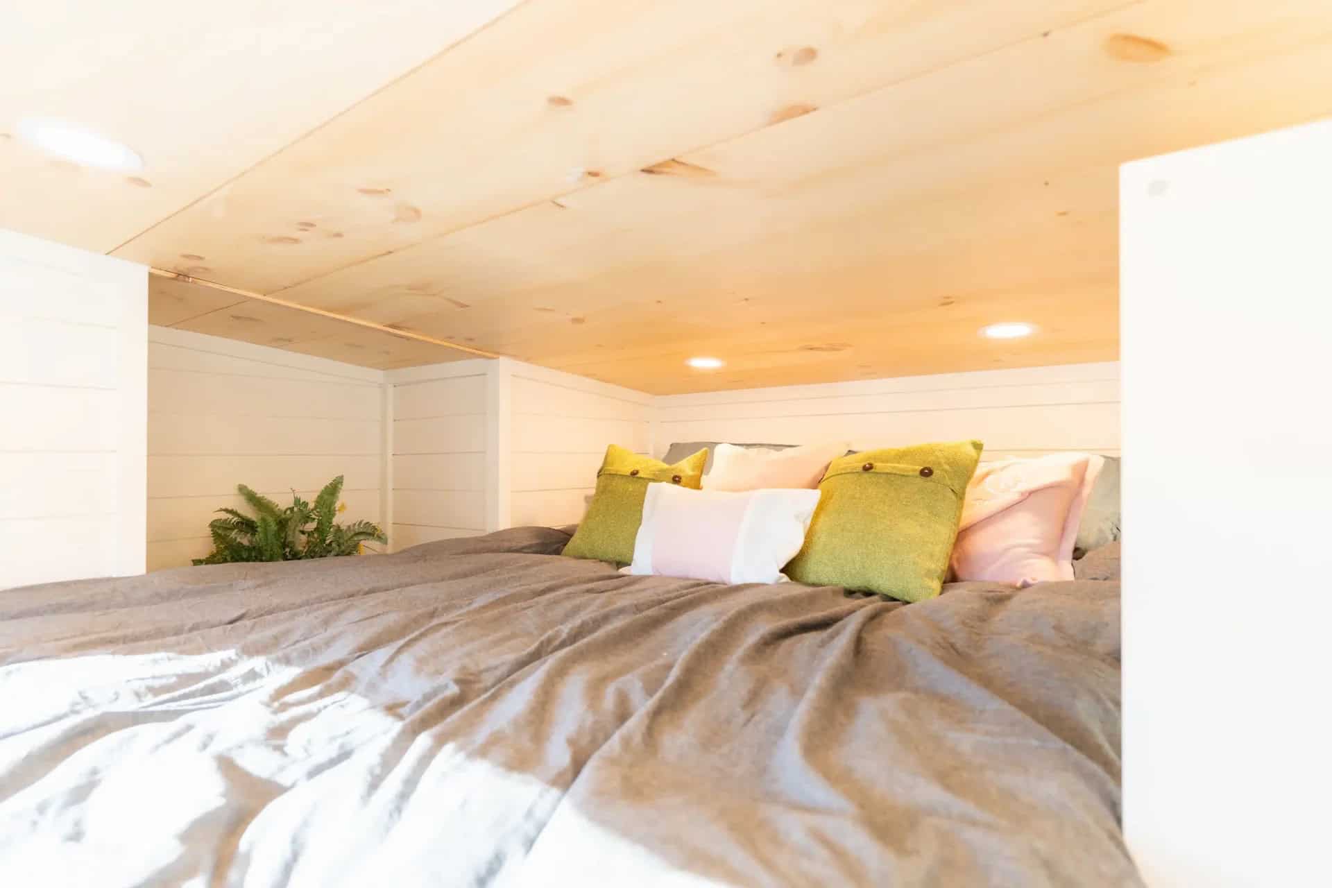 Genesis gallery loft: made bed with green and pink pillows under a knotty pine ceiling with recessed lights, white shiplap walls