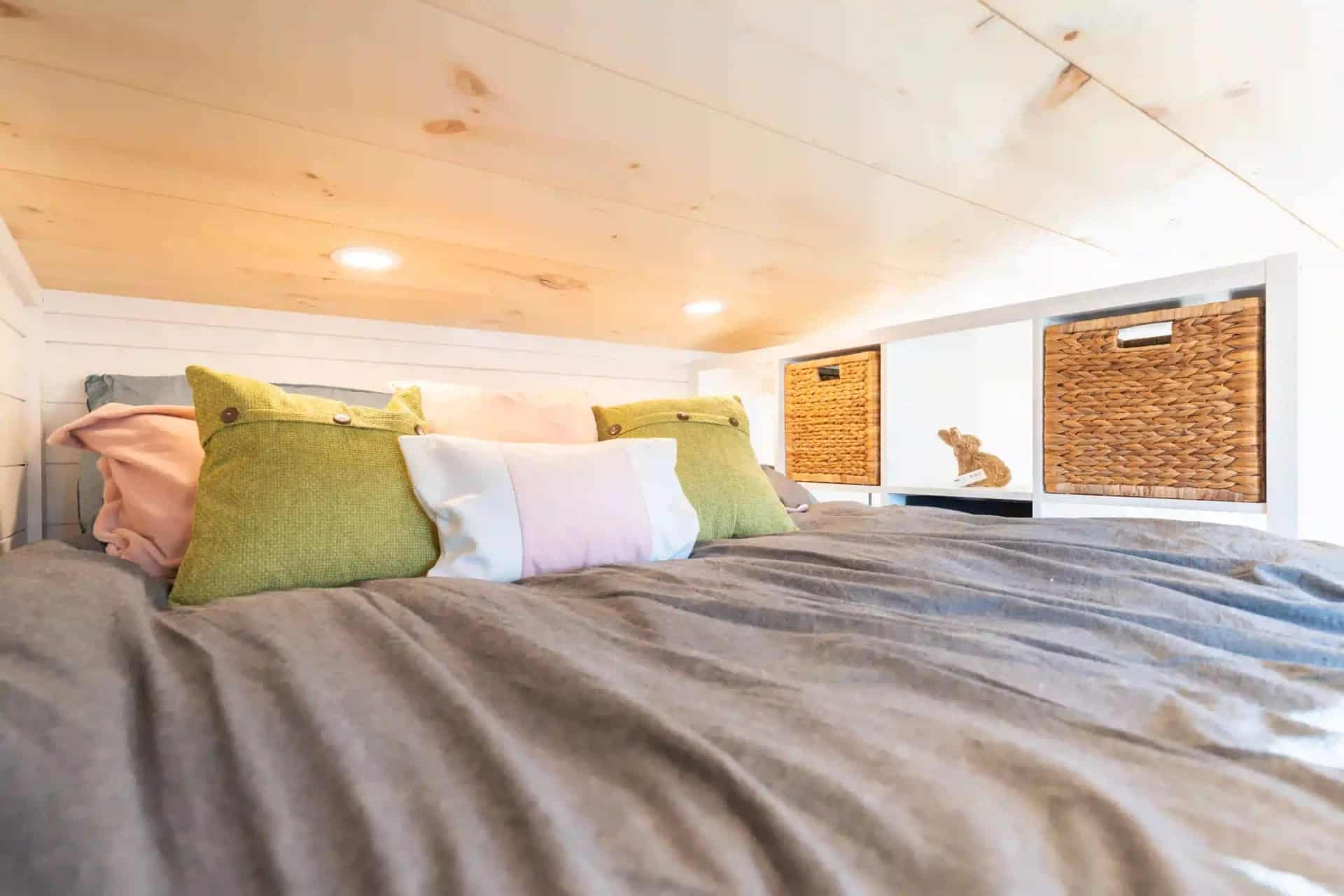 Genesis gallery loft: bed with pillows beside a built-in cubby wall holding woven storage baskets, pine ceiling above