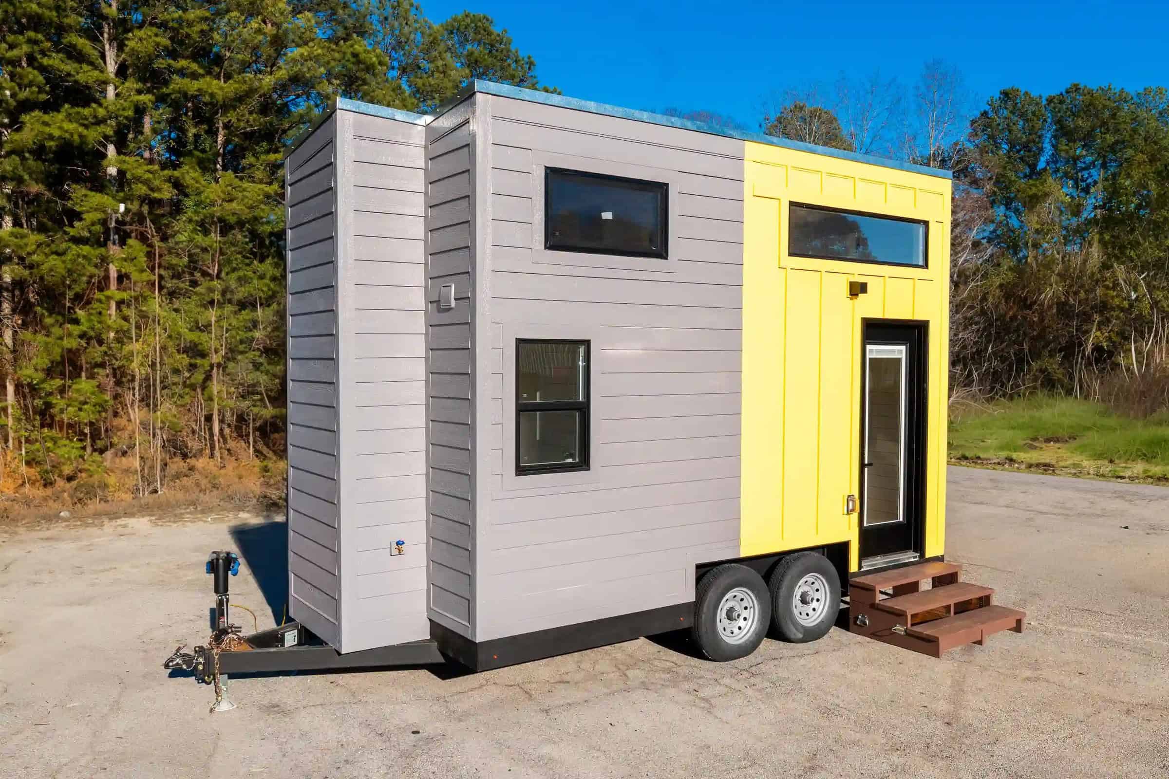 Grey and yellow 16-ft tiny house on a dual-axle trailer, black glass door with built-in blinds, wooden steps — Dragon Genesis gallery still
