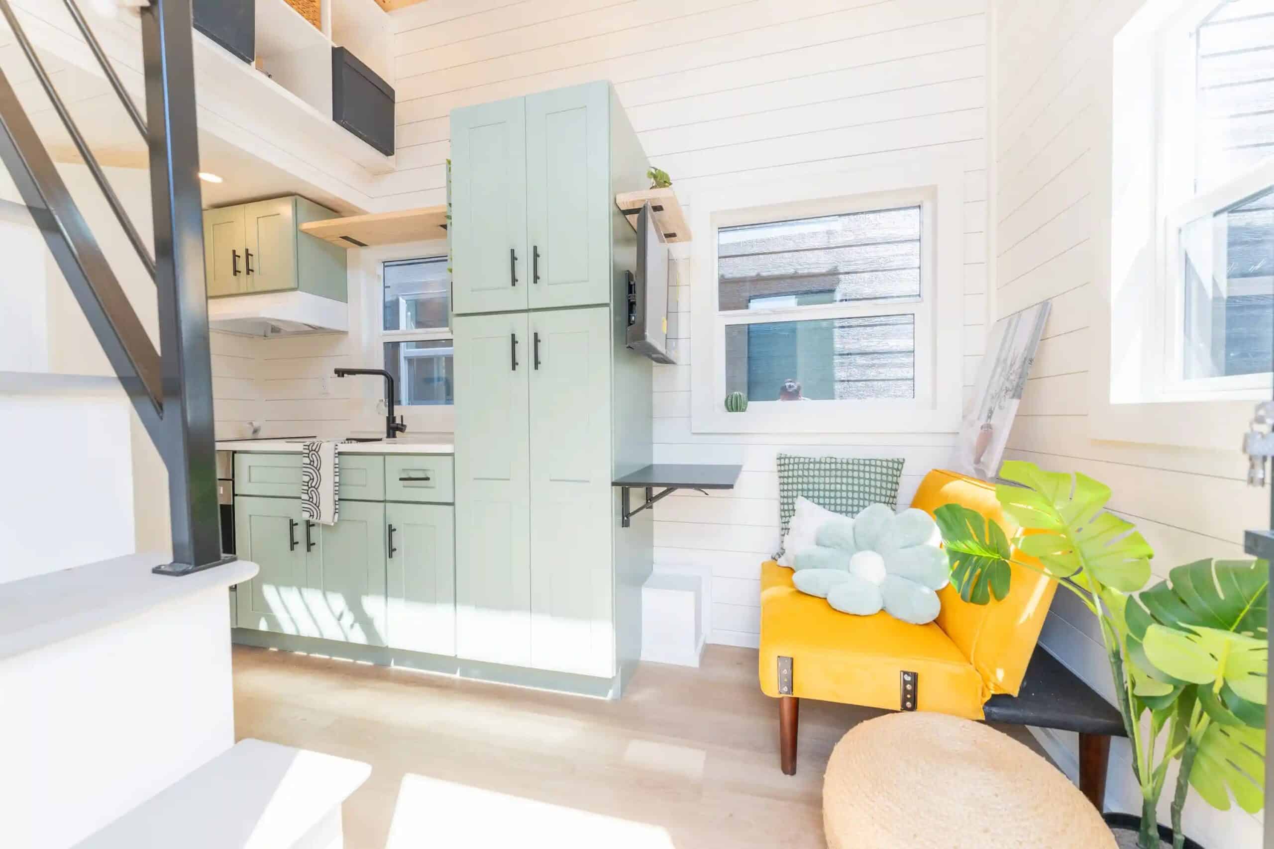 Genesis gallery interior looking down the length: mint kitchen and tall pantry on the left, wall-mounted TV, folding desk, yellow chair under the windows