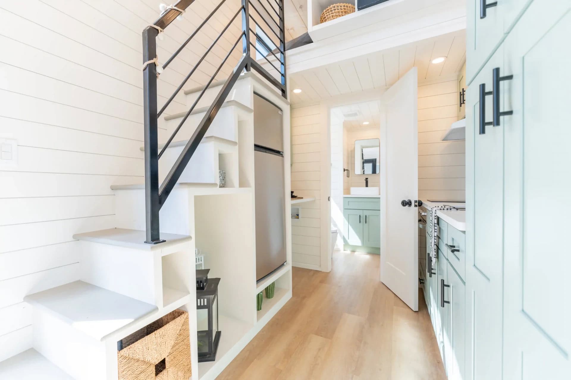 Genesis gallery interior: stairs with woven basket storage, full-height fridge tucked into the stair mass, hallway to the bathroom vanity beyond