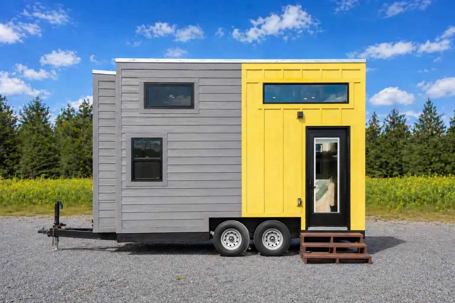 Dragon Genesis 16 listing lead: grey horizontal siding and yellow board-and-batten THOW on a dual-axle trailer, black glass door, wildflower field behind