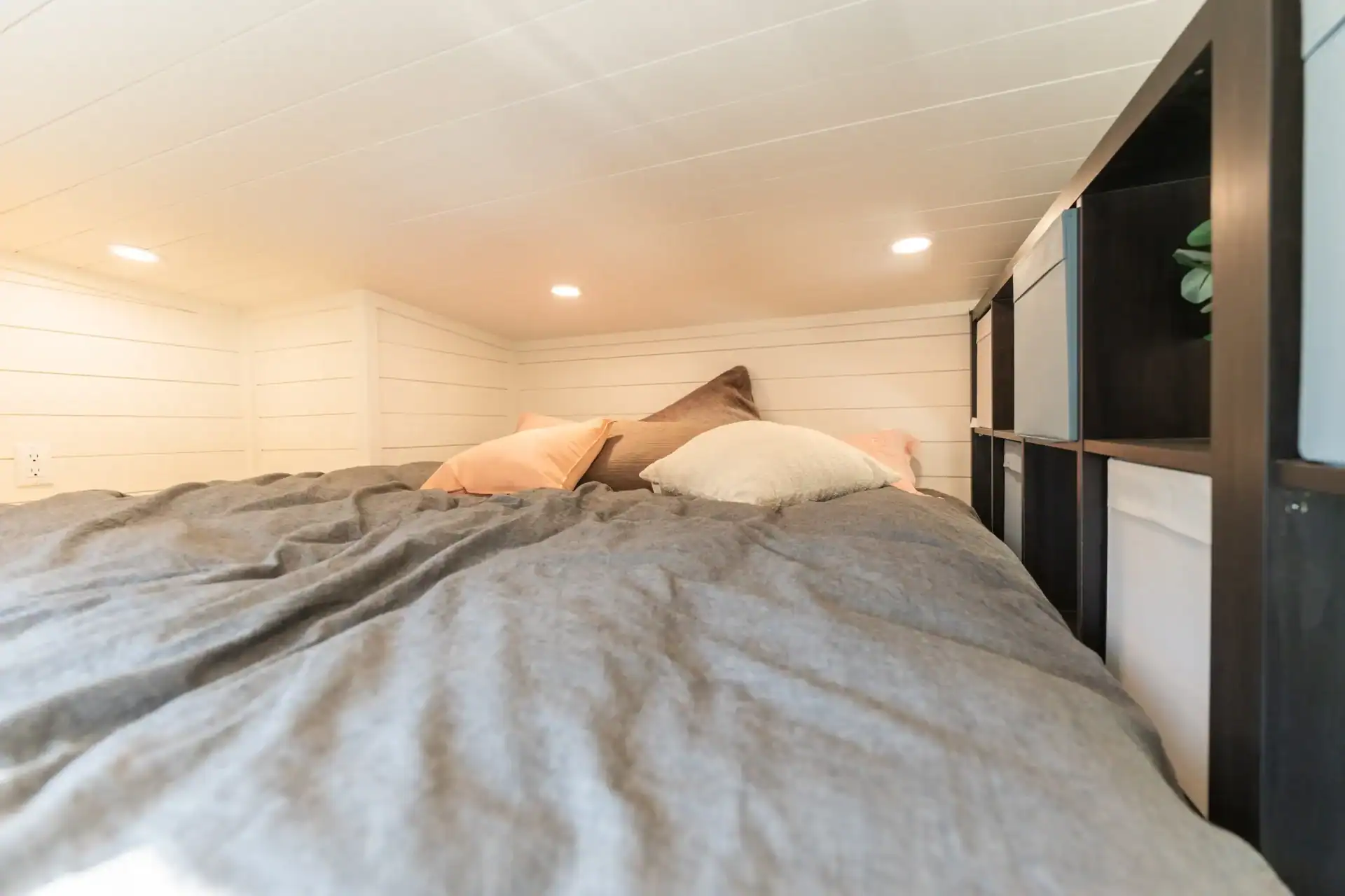 Sora sleeping loft: full-size bed under a low white-shiplap ceiling, three recessed lights, dark cubbie storage along the loft rail