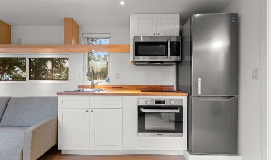Compact tiny house kitchen with modern appliances and white cabinetry.