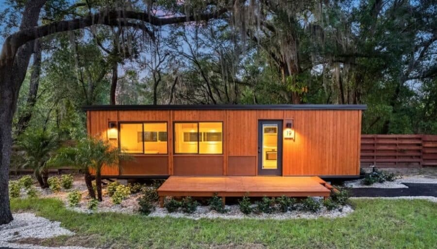 Cozy tiny house with warm lighting nestled among trees in a peaceful natural setting.