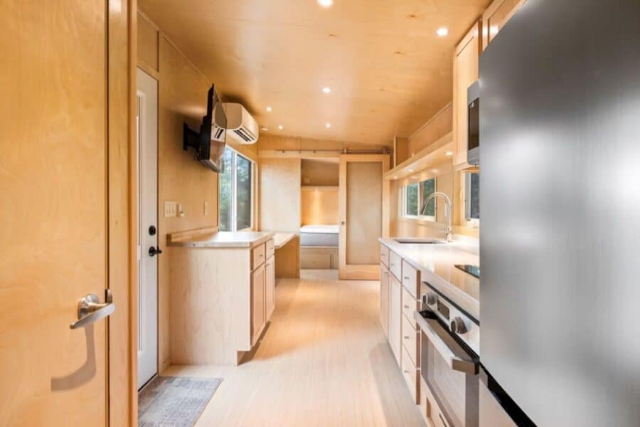 Compact tiny house kitchen with modern appliances and natural wood finishes.