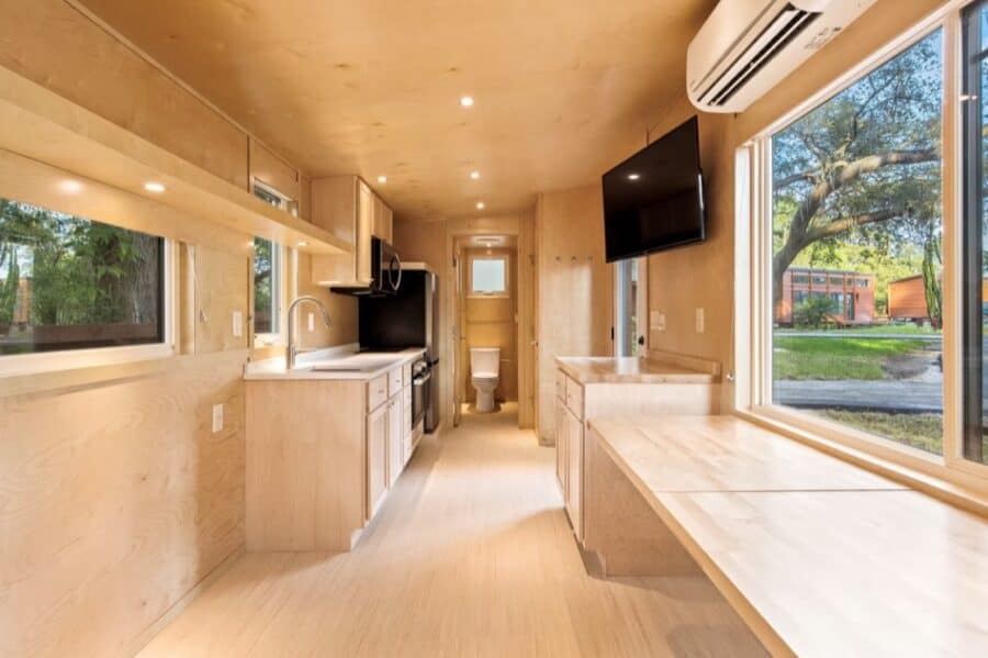 Compact tiny house kitchen with modern appliances and large windows.