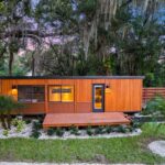 Tiny house with wooden exterior and large windows in a green garden setting.