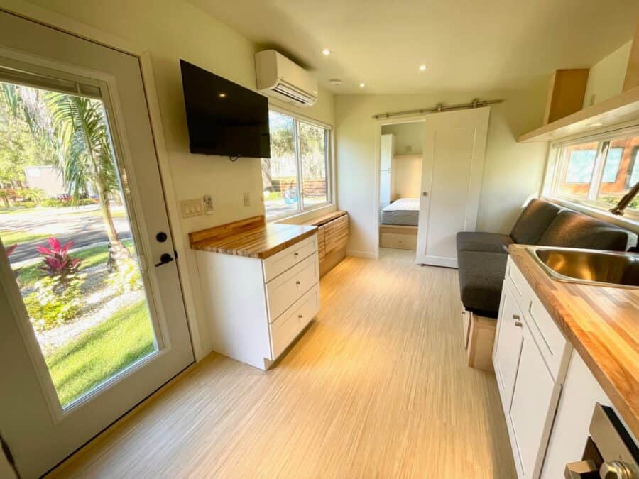 Compact tiny house kitchen with white cabinets, wooden countertops, and large windows for natural li.