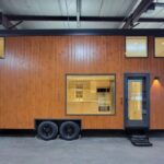 Modern tall tiny house on wheels with wooden exterior and large windows.