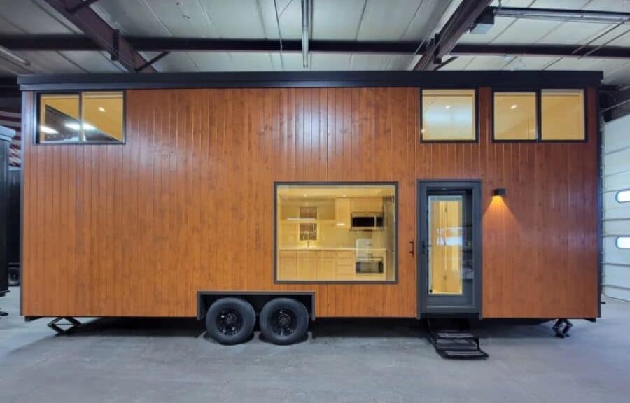 Modern tall tiny house on wheels with wooden exterior and large windows.