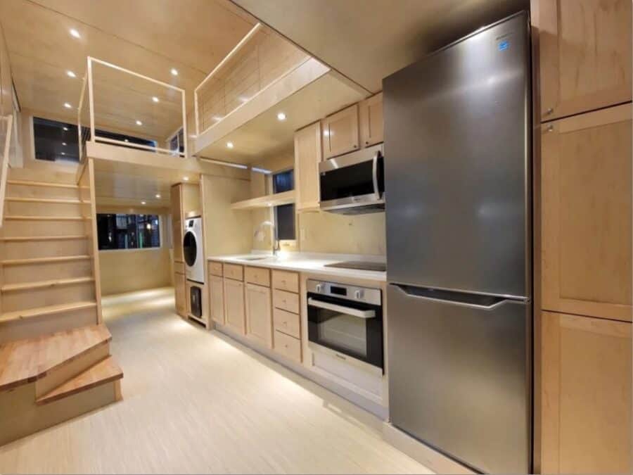 Modern tiny house kitchen with sleek appliances and wooden cabinetry.