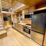 Modern tiny house kitchen with wood finishes, appliances, and loft space.