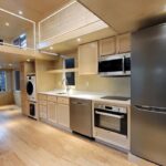 Bright, minimalist tiny house kitchen featuring stainless steel refrigerator, oven, microwave, and w.