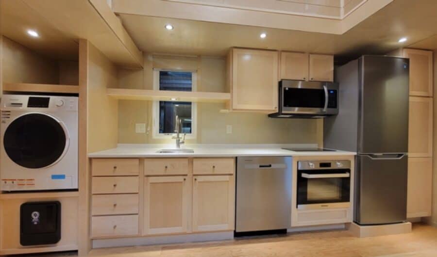 Compact tiny house kitchen featuring washer, fridge, microwave, and oven appliances.